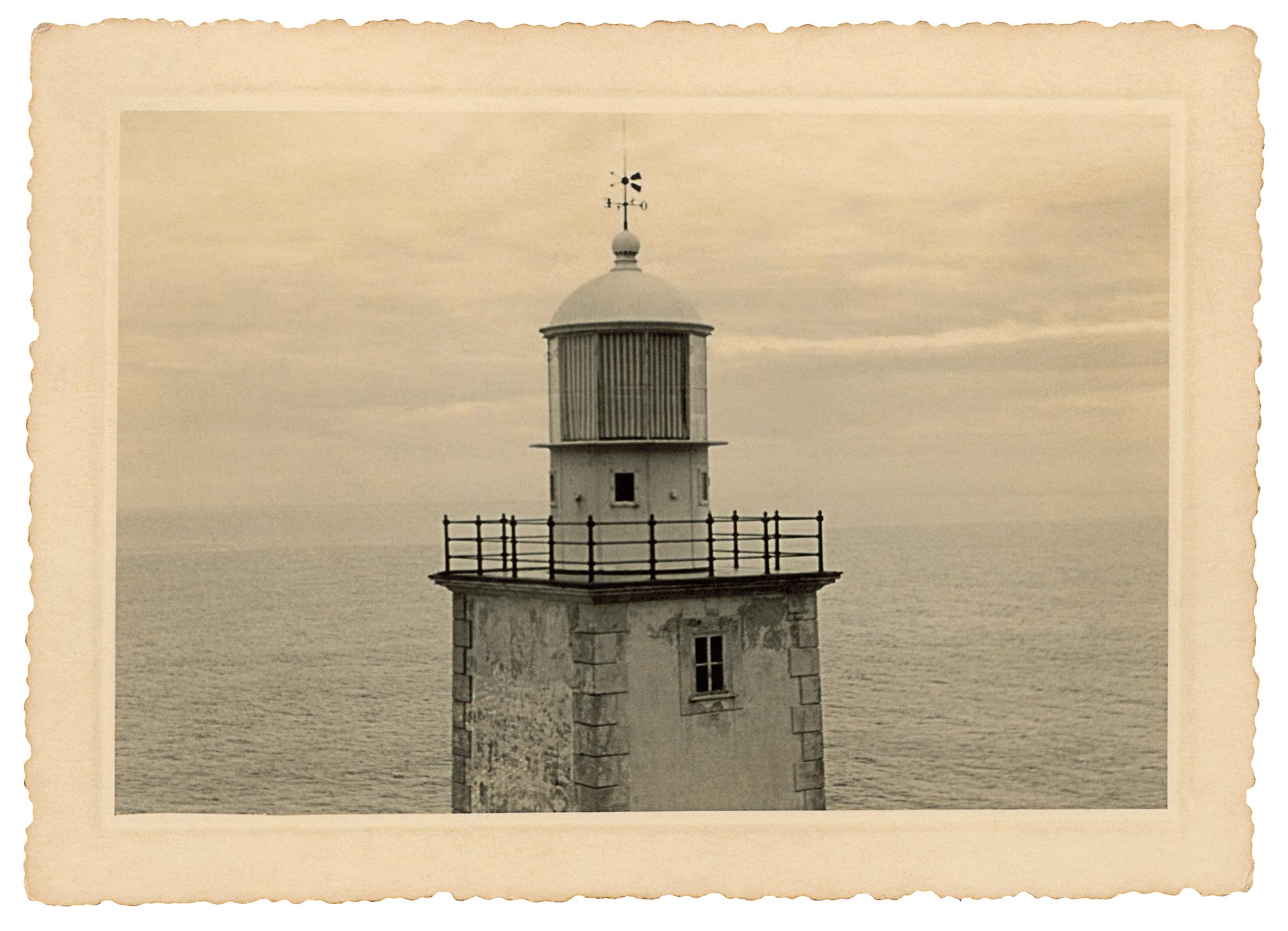 Foto em preto e branco com um farol de sinaliza&ccedil;&atilde;o mar&iacute;tima bem no centro da imagem. Ao fundo, o oceano e o c&eacute;u.