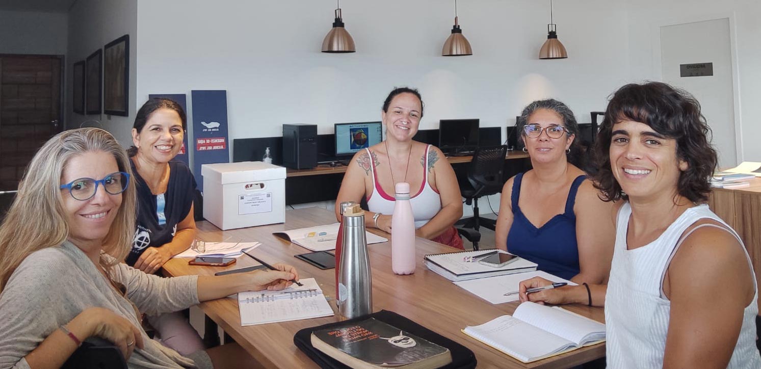 Na Casa do Patrim&ocirc;nio, uma parte da equipe do projetor formada por cinco mulheres est&aacute; sentada ao redor de uma mesa. Todas olham para frente sorrindo.