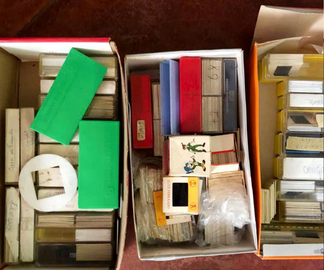 Fotografia mostra tr&ecirc;s caixas de sapato dispostas lado a lado contendo v&aacute;rias caixinhas de slides, molduras e slides soltos.