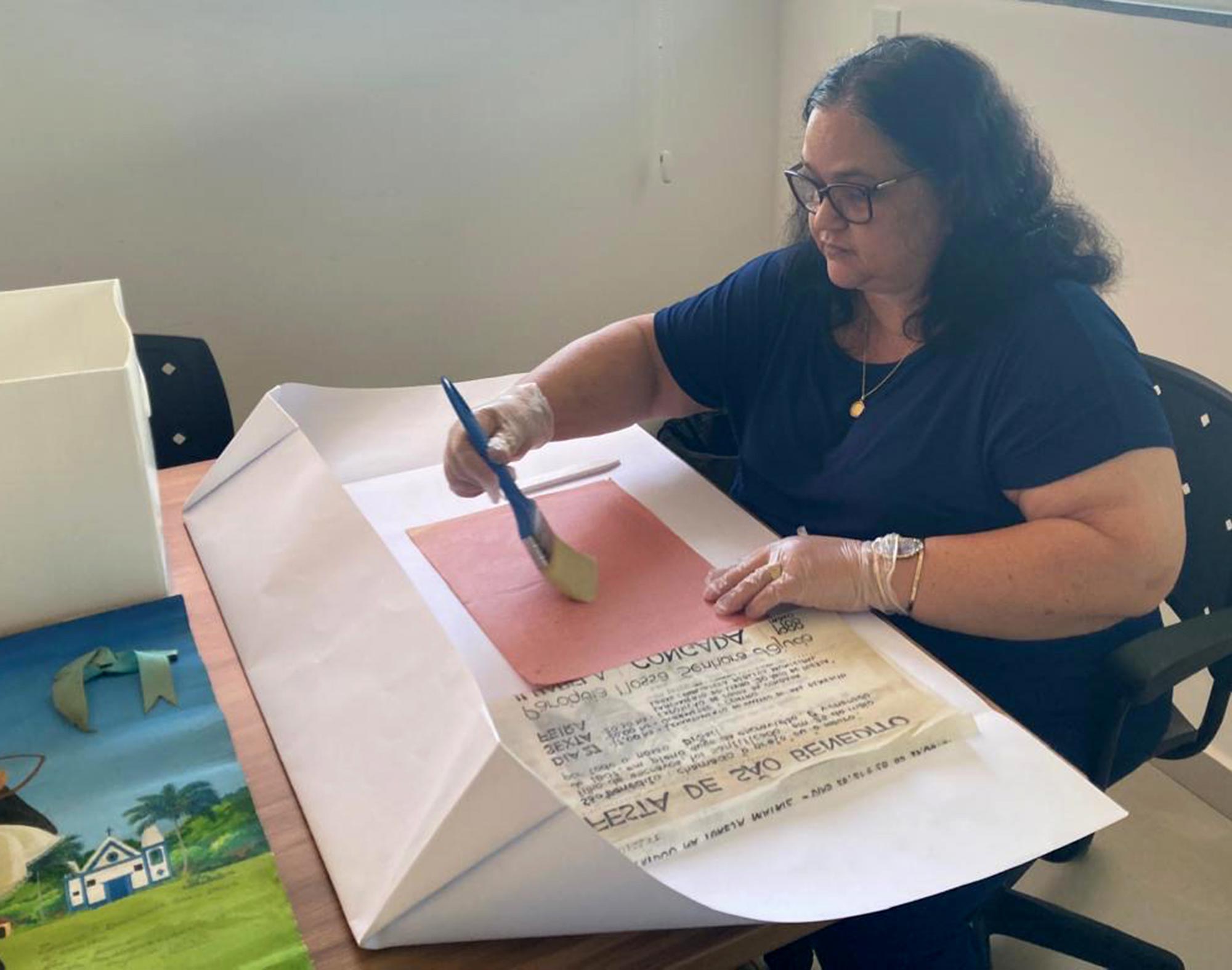 Arquivista da casa do Patrim&ocirc;nio veste luvas e manuseia um documento antigo com um pincel, utilizado para remover sujeira e poeira.