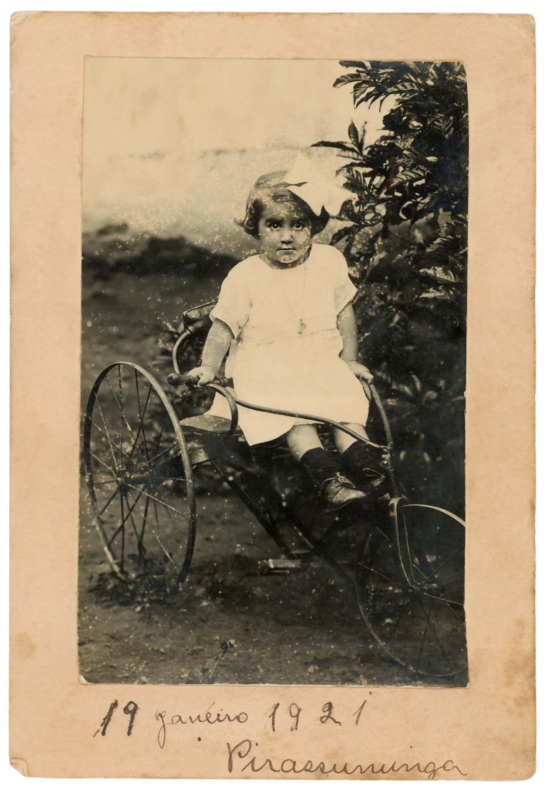 Foto antiga e desbotada, em preto e branco, mostra Ded&eacute; em cima de um carrinho de metal. Na parte de baixo da foto est&aacute; escrito a m&atilde;o: 19 de janeiro de 1921.